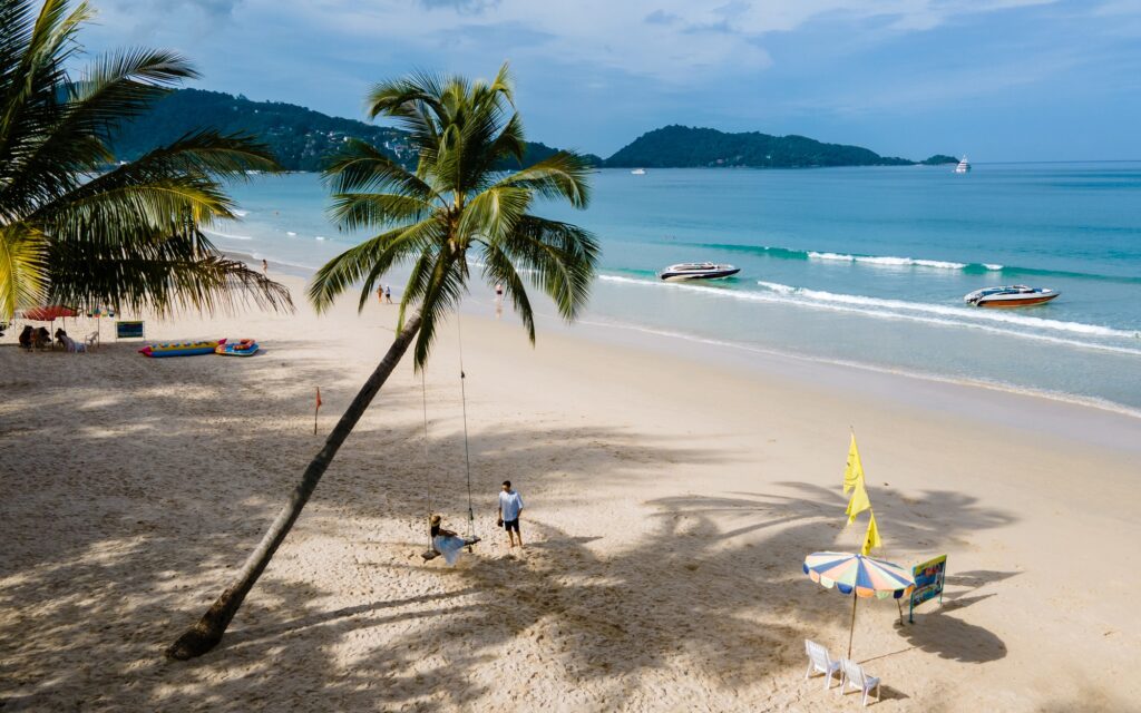 12 Enchanting Beaches in Thailand You Must Explore 2 A couple of men and women on a swing under a palm tree at the beach of Patong Phuket Thailand