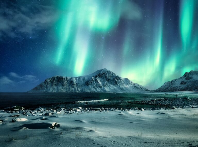 Aurora borealis, Northern lights over snow mountain range on coastline at Skagsanden beach