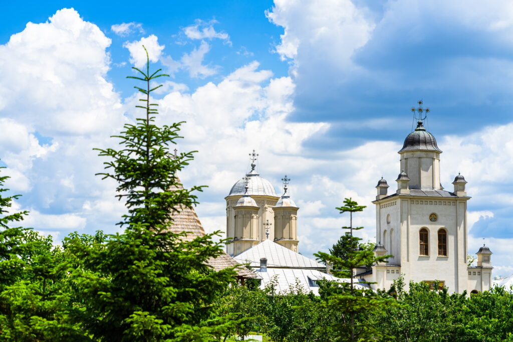 10 Enchanting Destinations You Must Discover in Romania 4 Orthodox church monastery near Bucharest, Romania surrounded by green trees under a cloudy sky